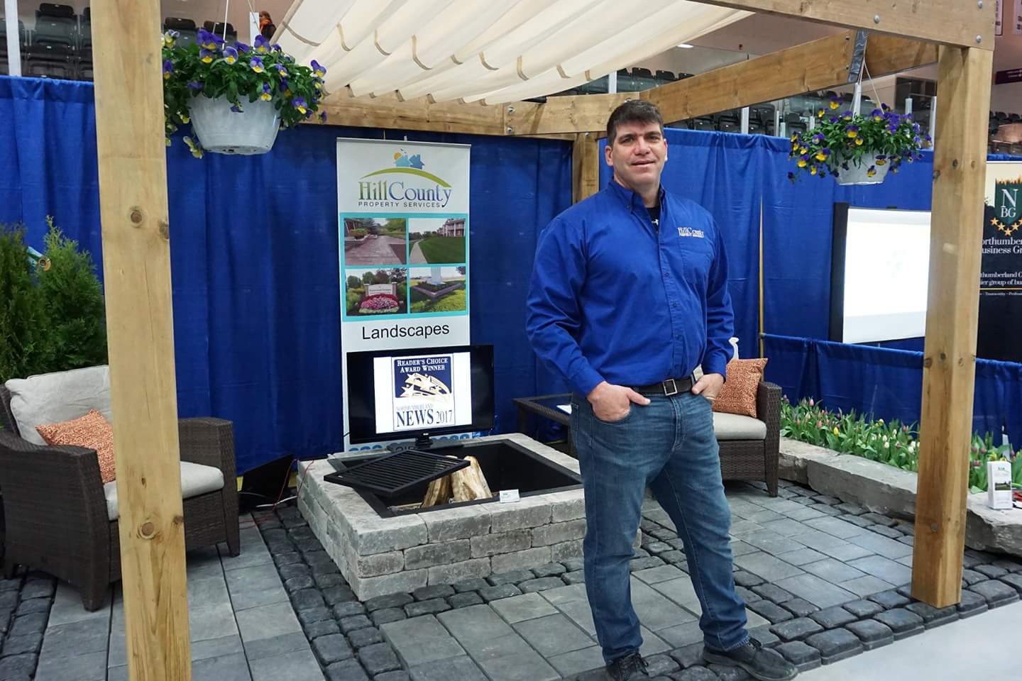Man at outdoor landscape booth with pergola and greenery.