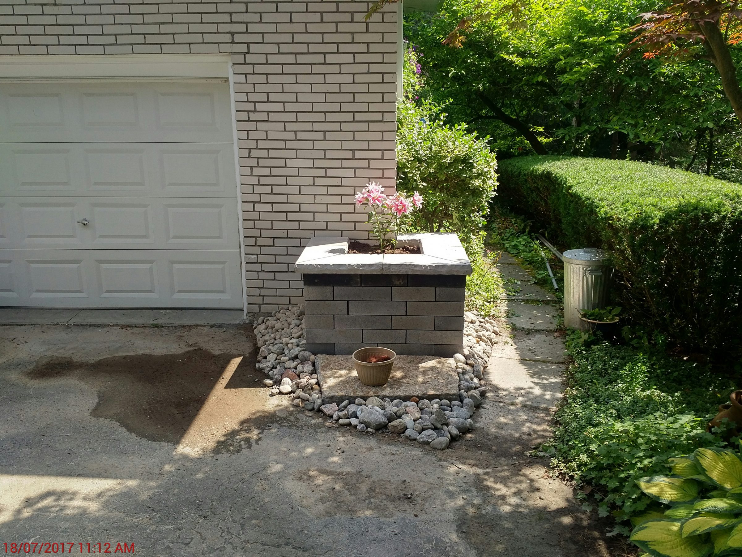 Brick planter with pink flowers by garage wall.