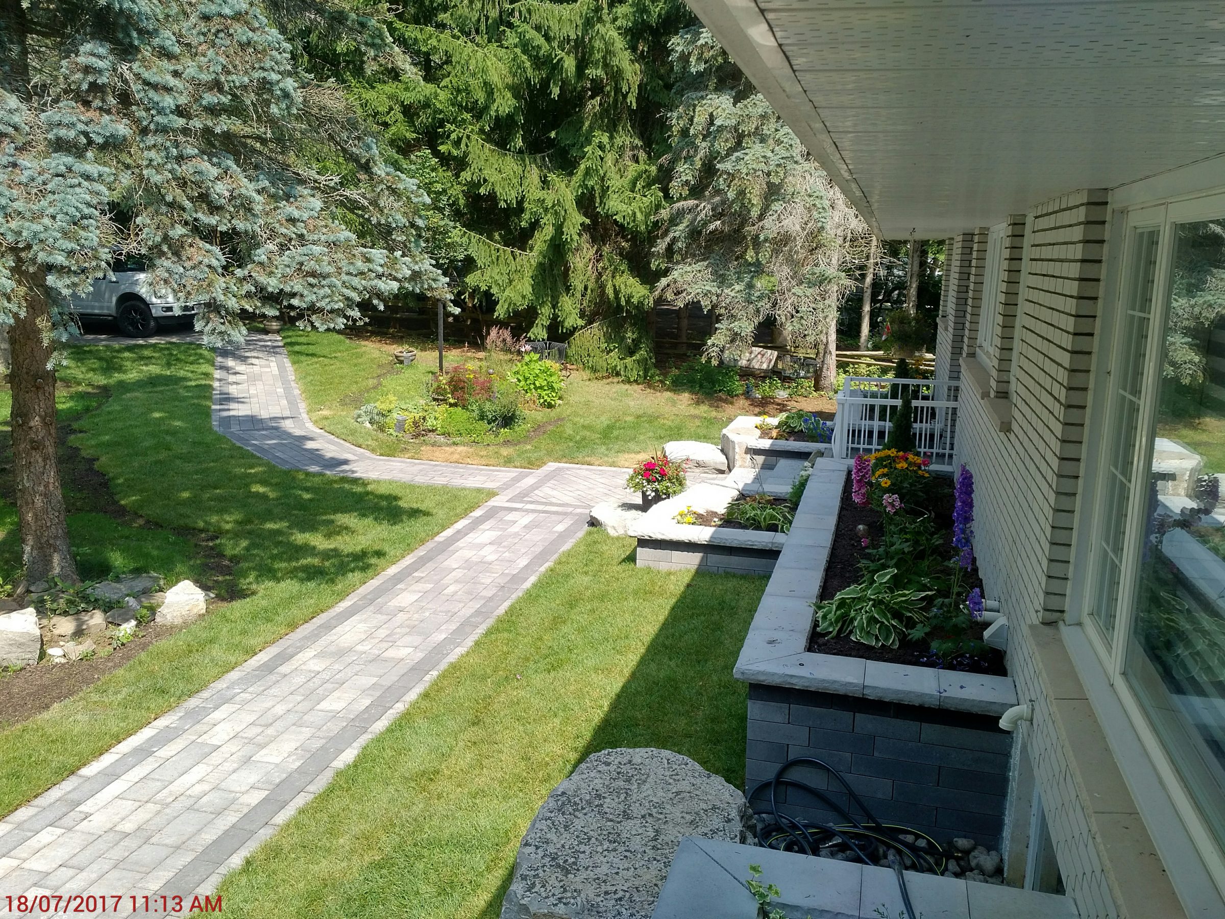 Brick pathway in garden with flowers and trees.