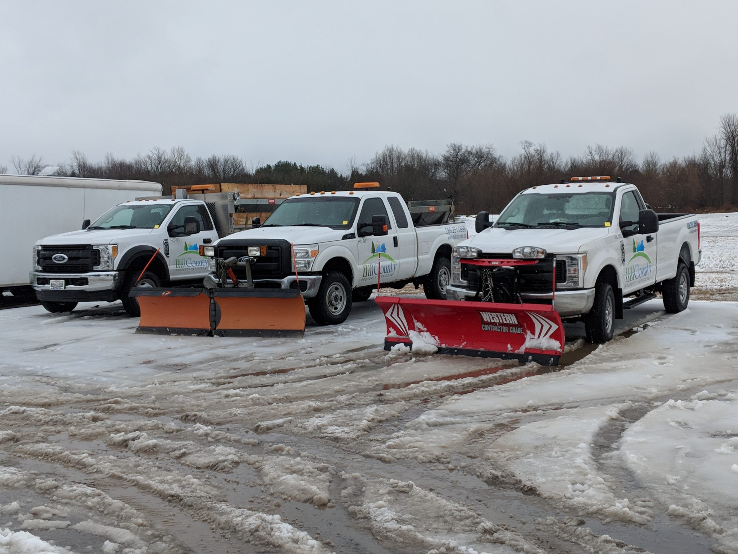 Three snow plow trucks in snowy parking lot.