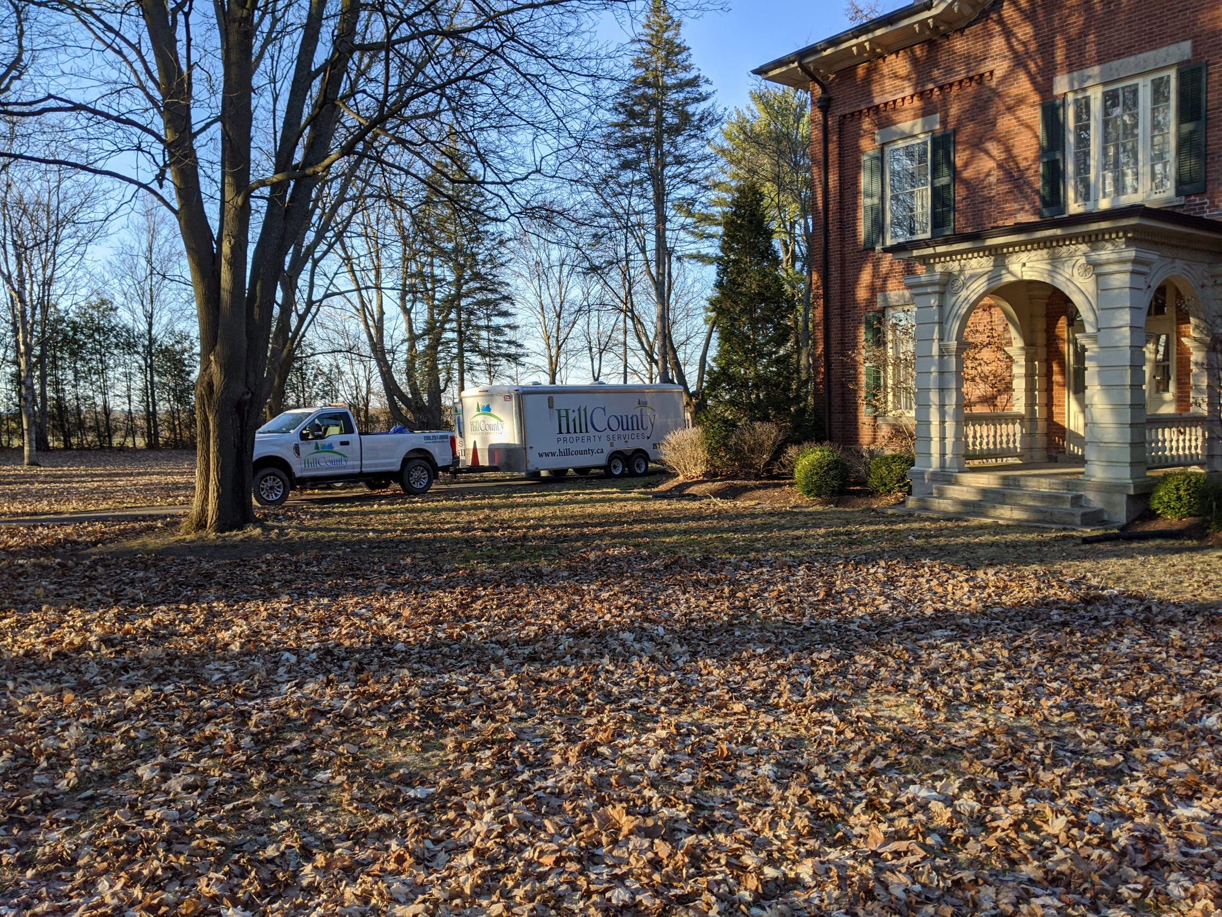 Truck and trailer parked near brick building, autumn leaves.