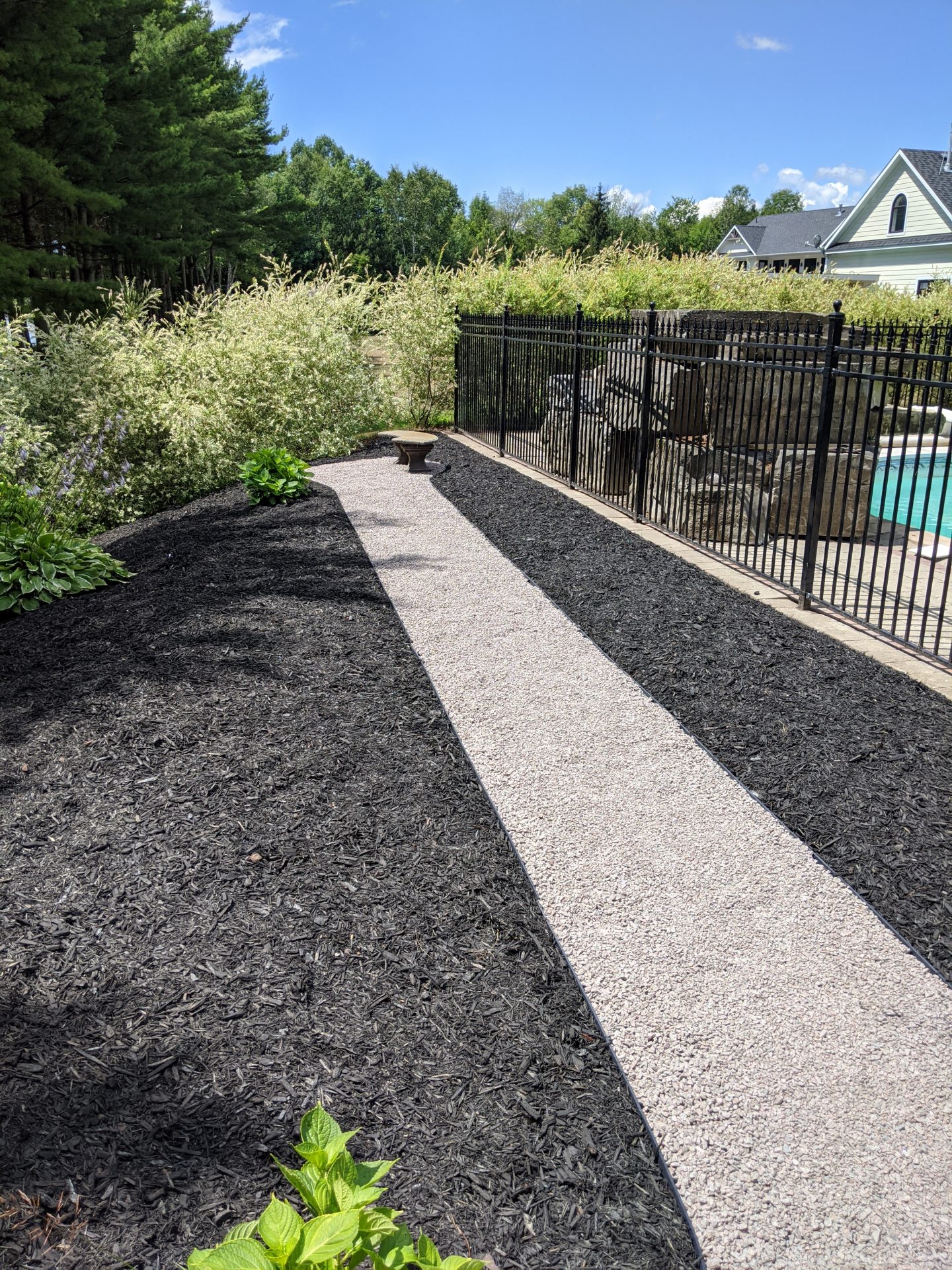 Gravel path beside pool with black mulch.