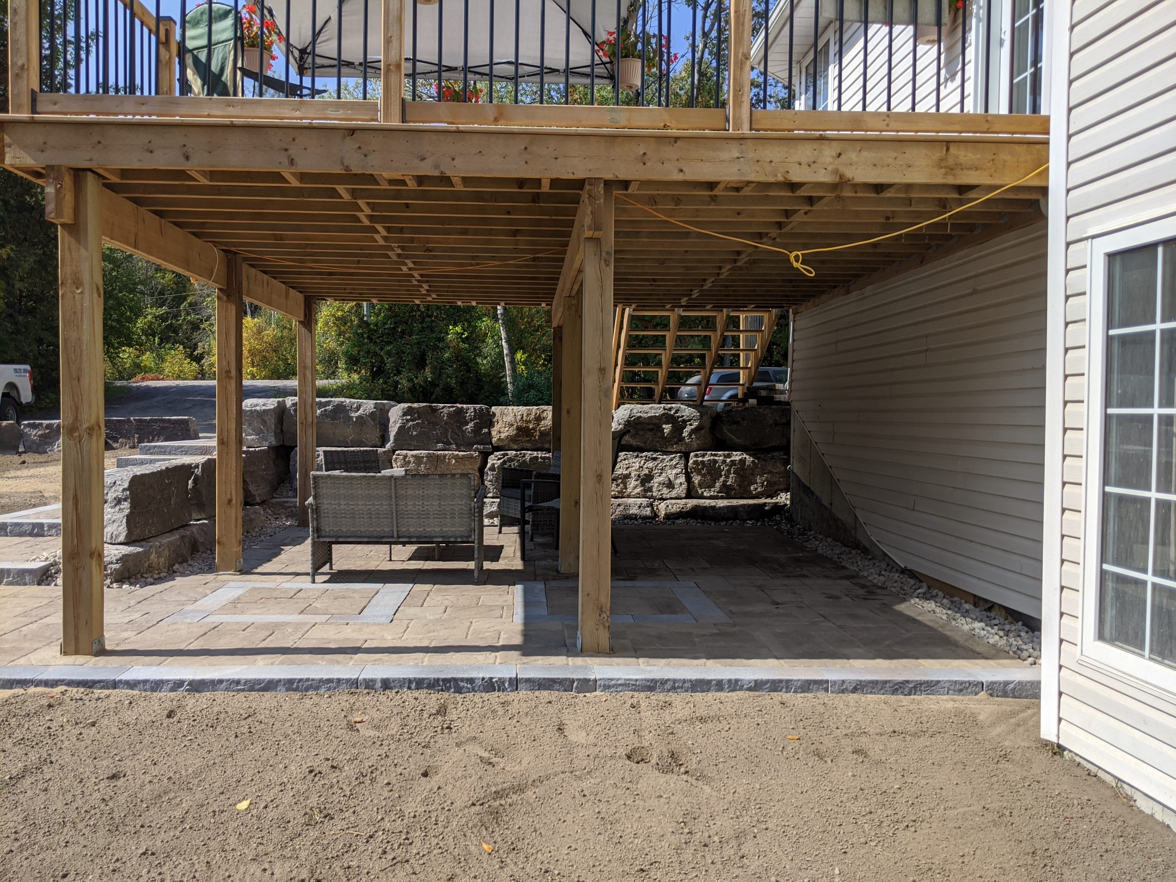 Outdoor patio under wooden deck with stone walls.