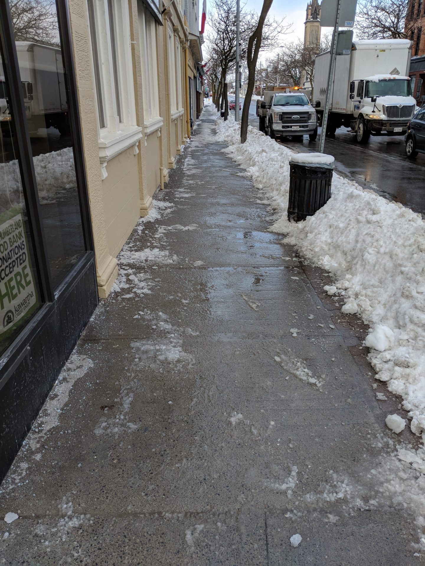 Icy sidewalk with piled snow on street edge.