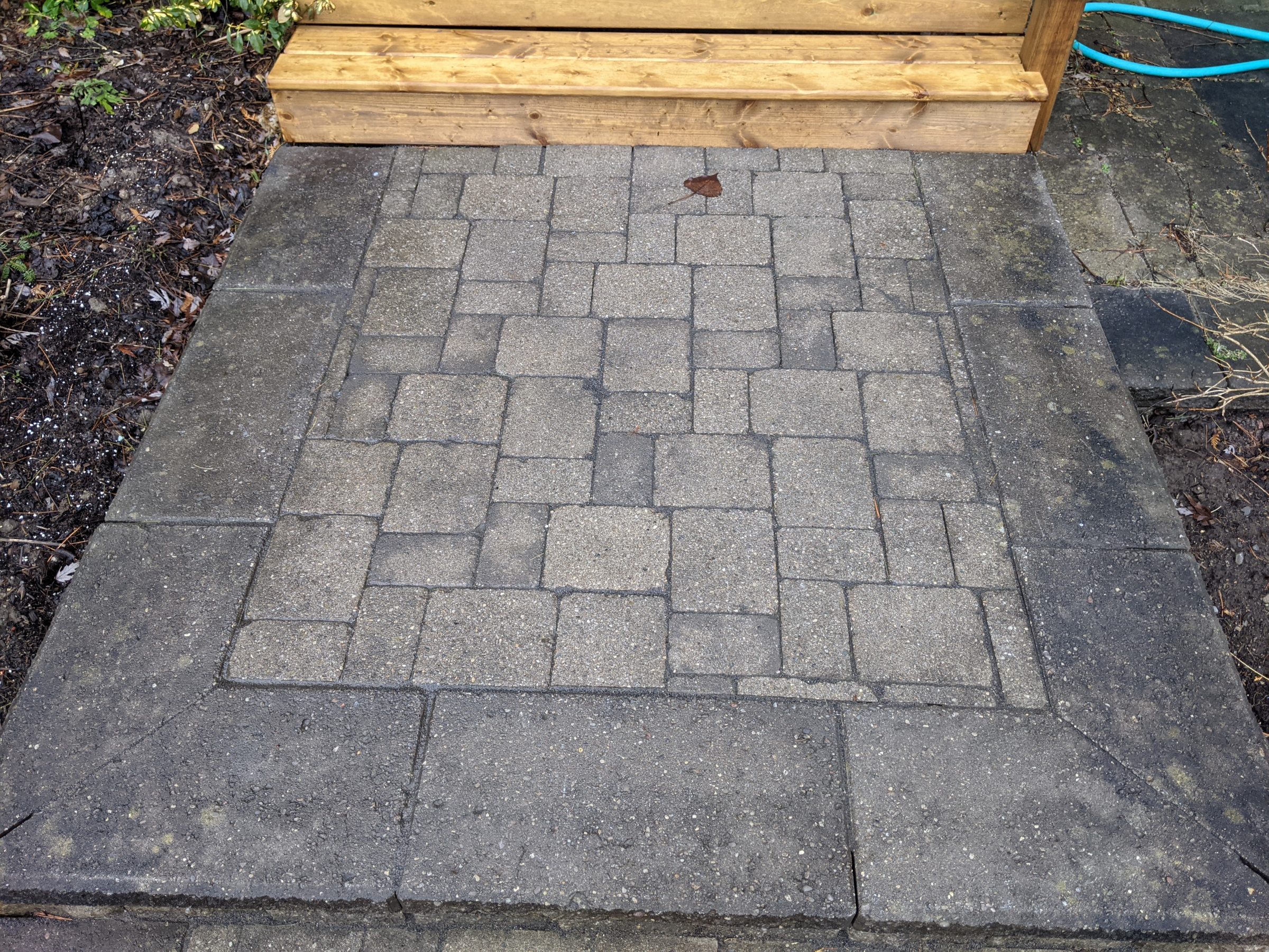 Stone patio beneath wooden steps with exposed soil.