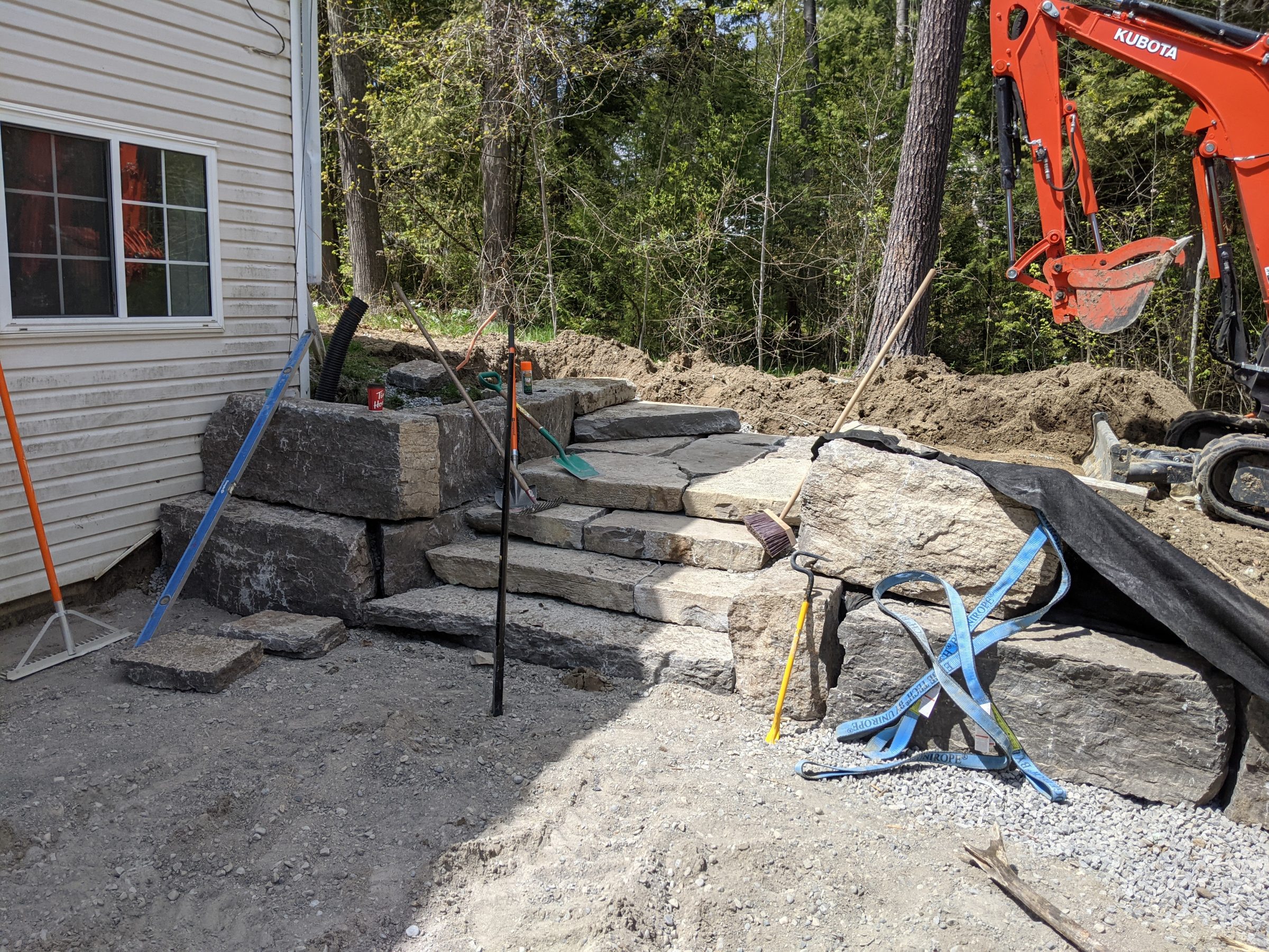 Backyard stone retaining wall under construction with excavator.