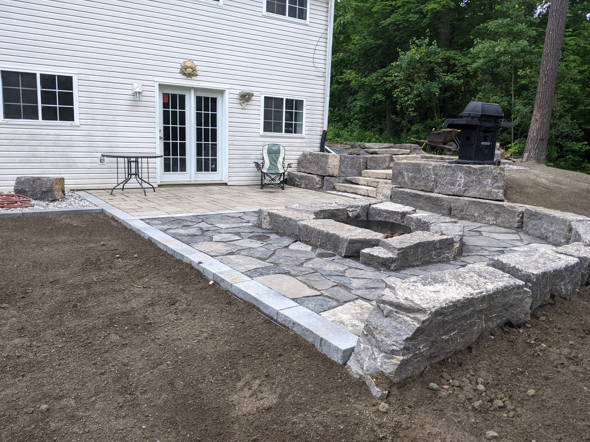 Stone patio with steps and grill in backyard.
