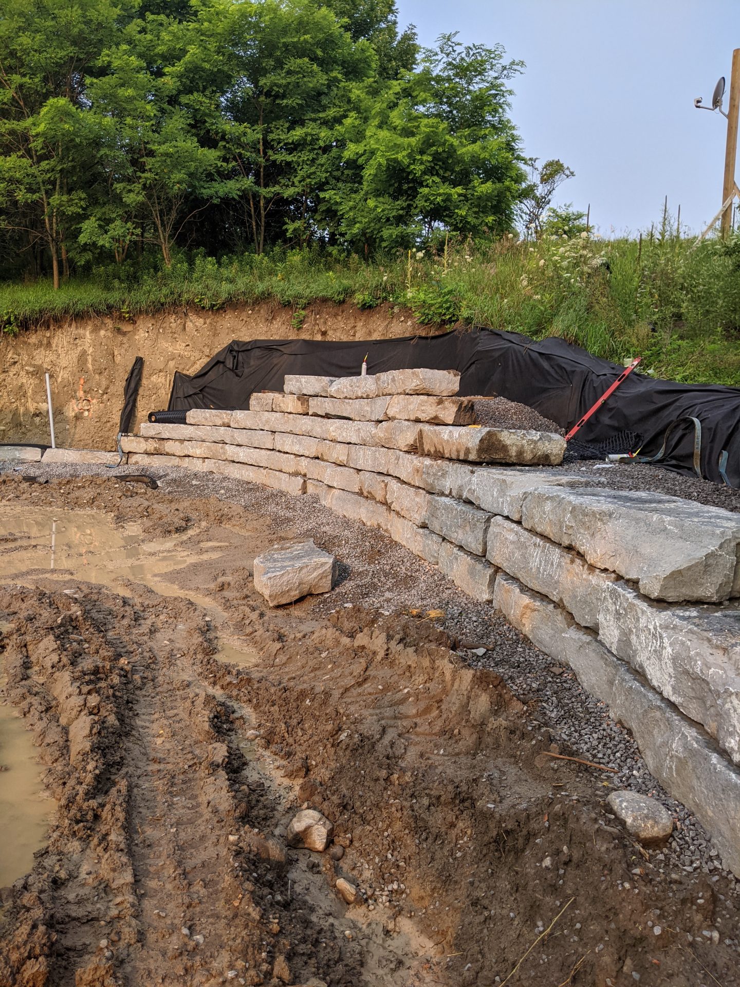 Stone retaining wall under construction with muddy path.