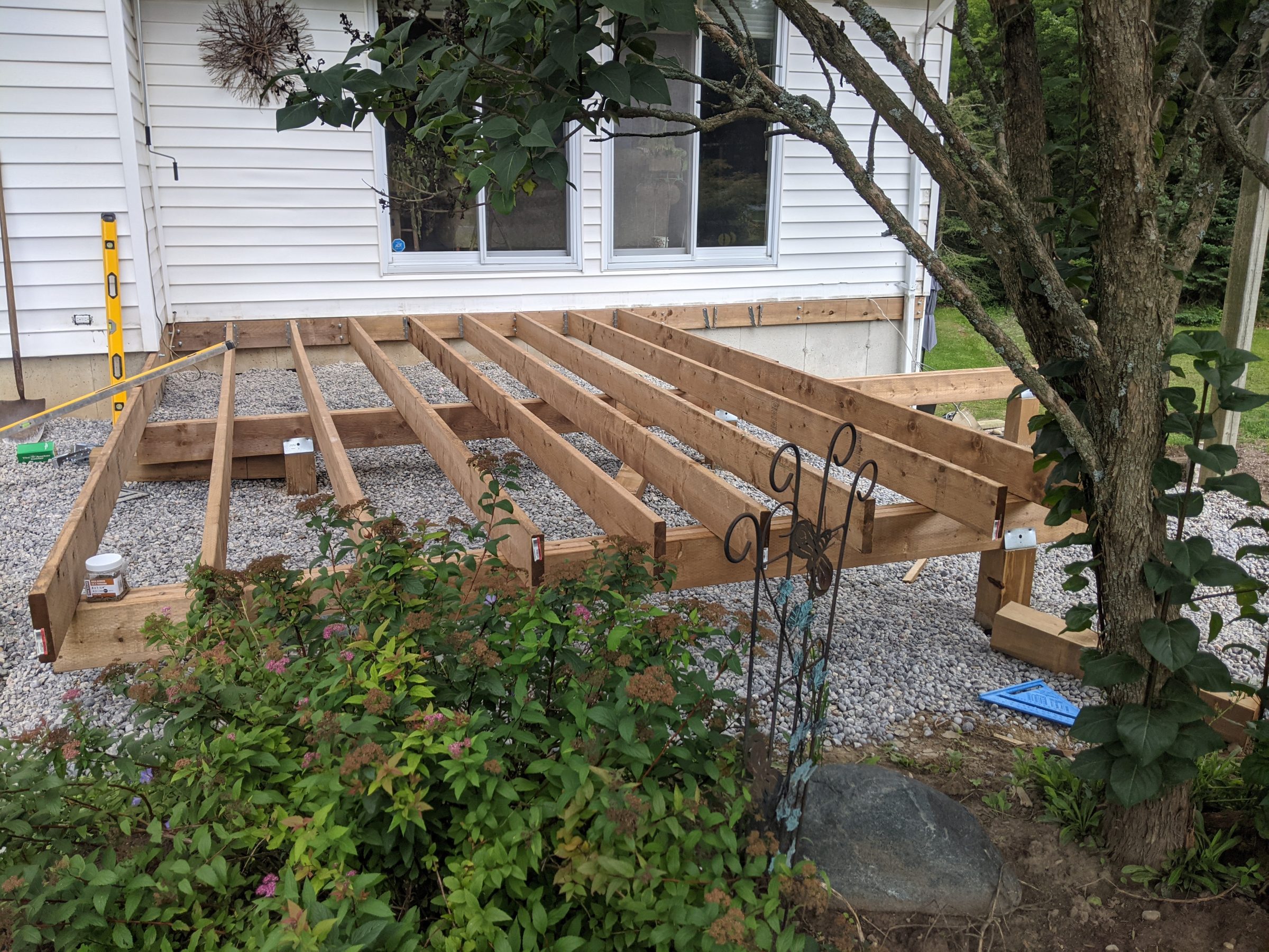 Wooden deck frame under construction beside white house.