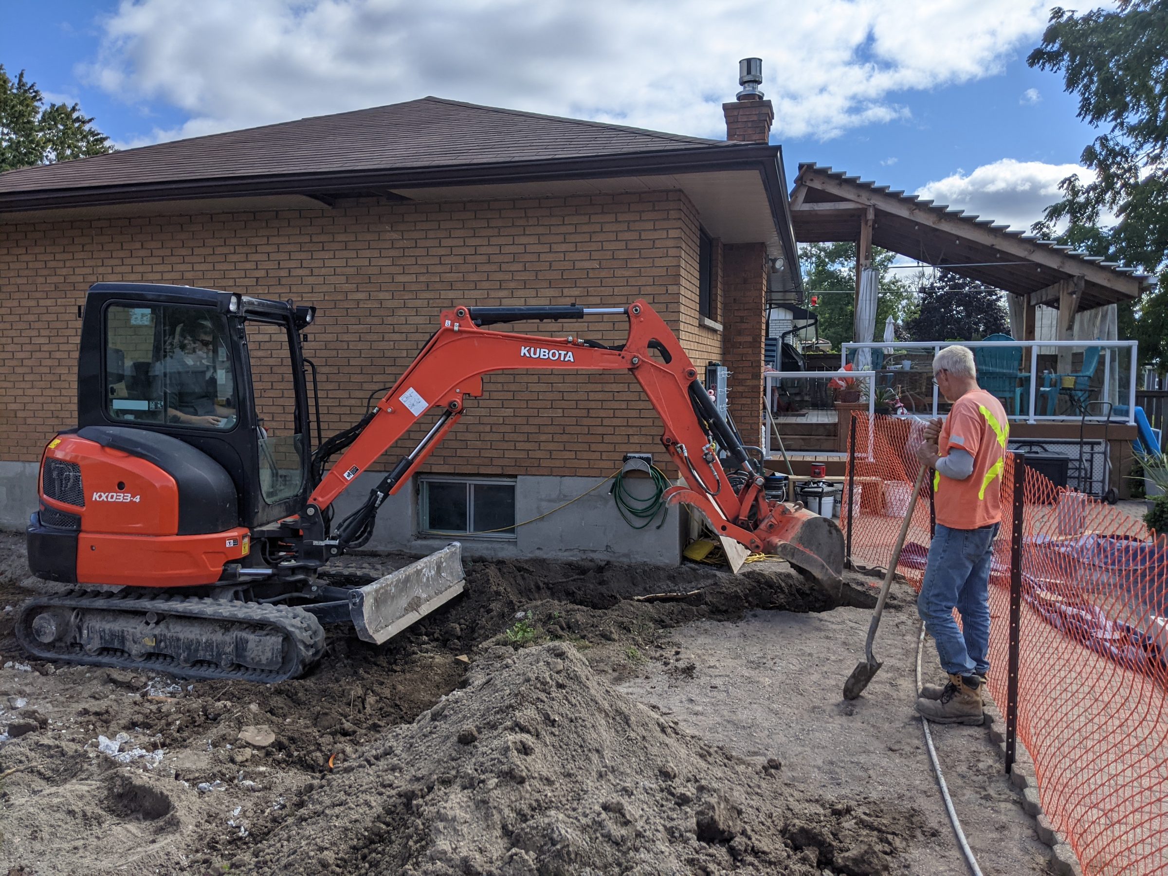Worker guiding excavator near house construction site.