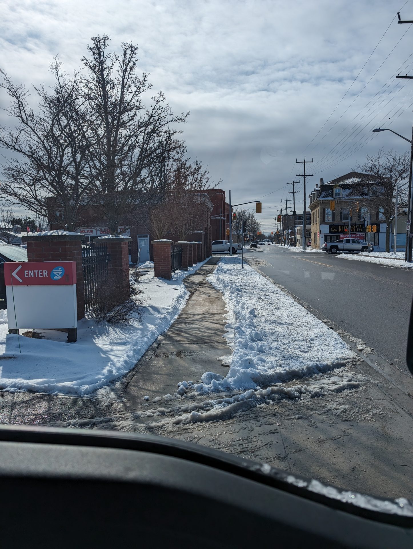 Snowy sidewalk and street with bare trees