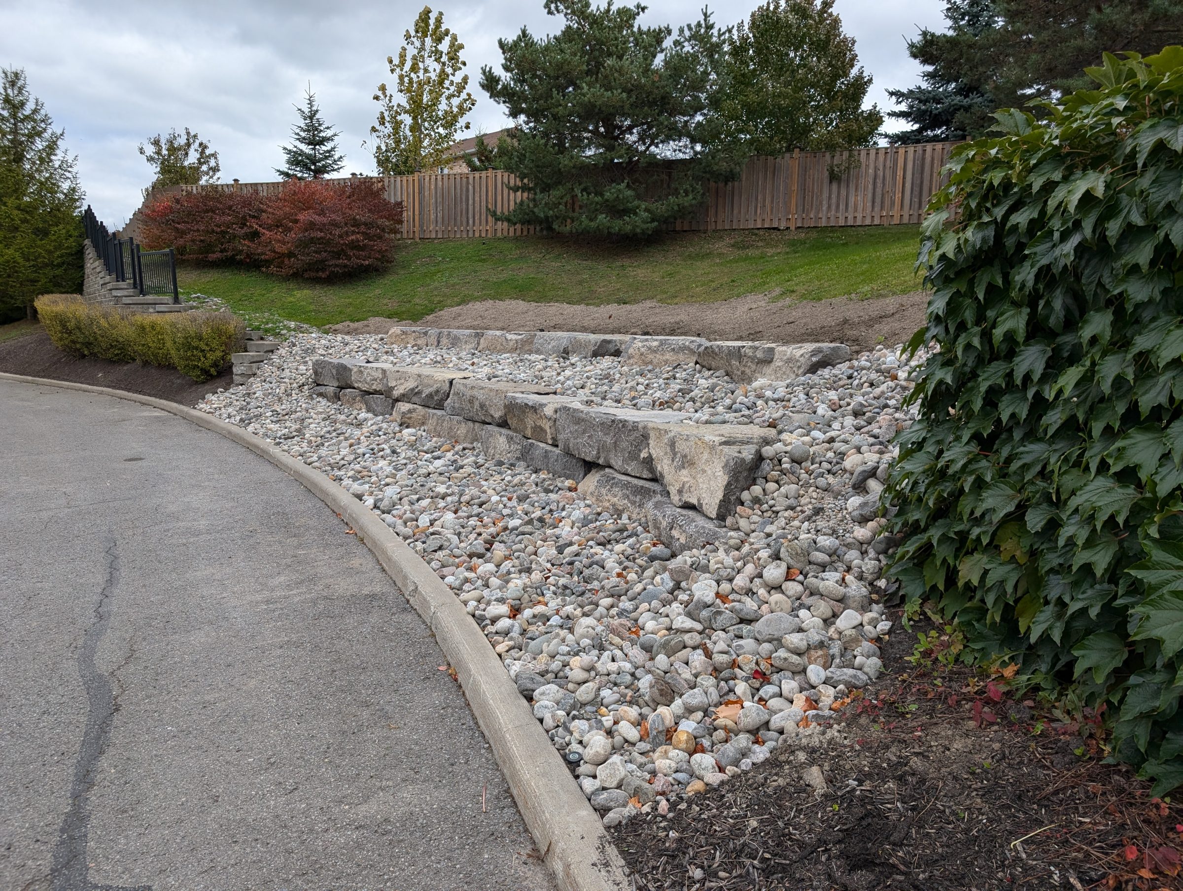 Paved path beside landscaped rock garden with trees.