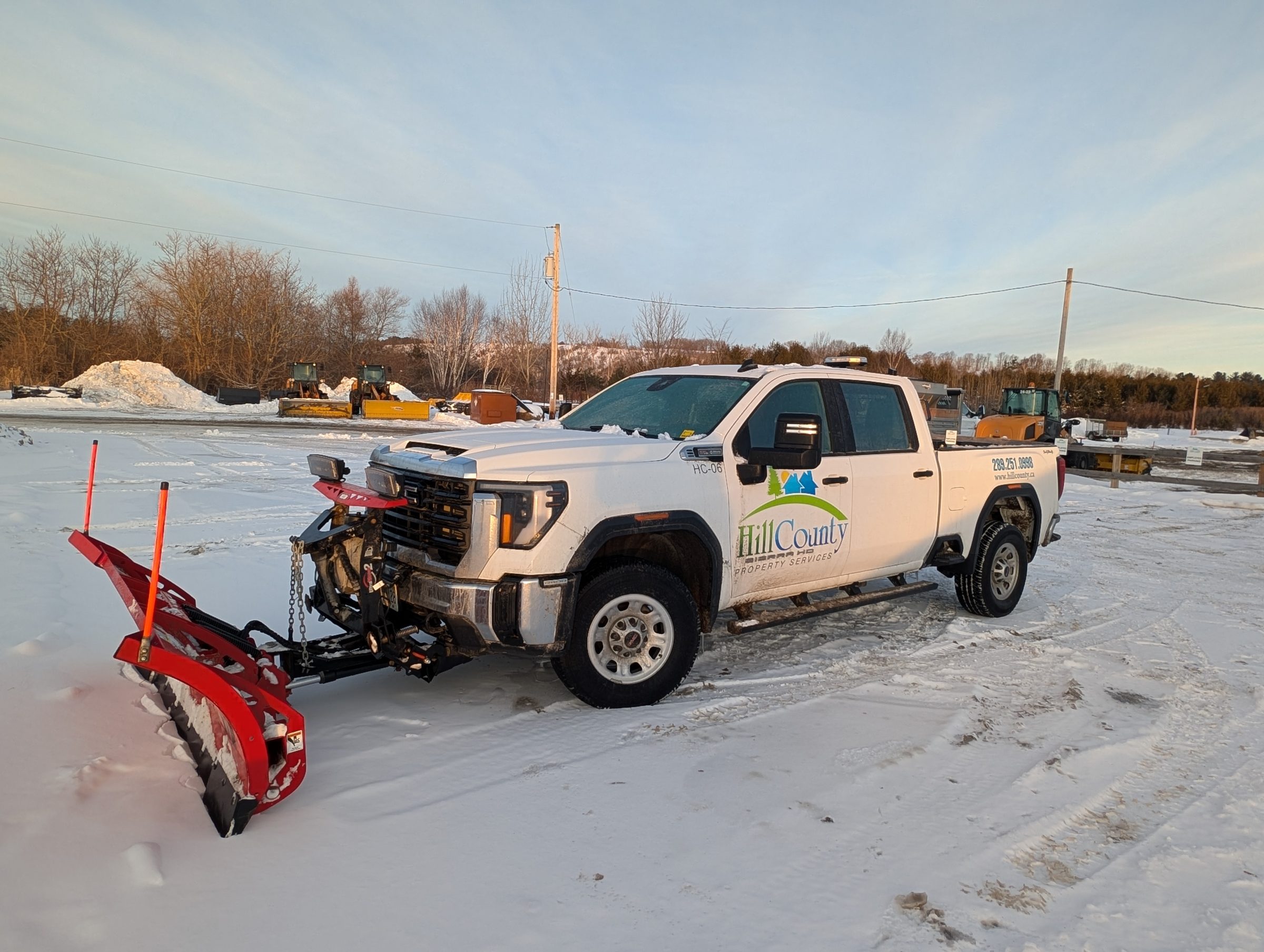 Snow plow truck on snowy lot at sunset.