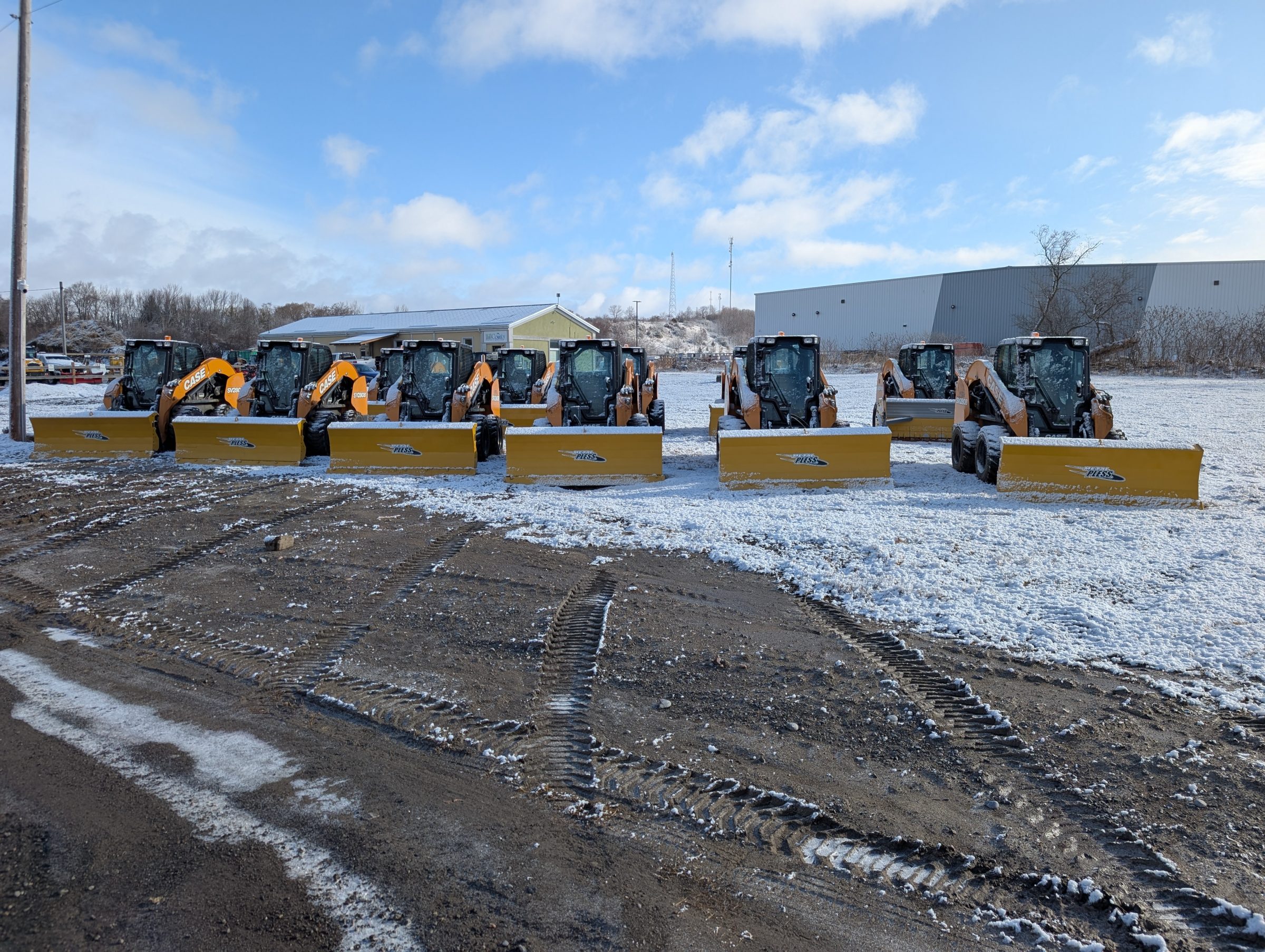 Six snowplows in a snowy parking lot.
