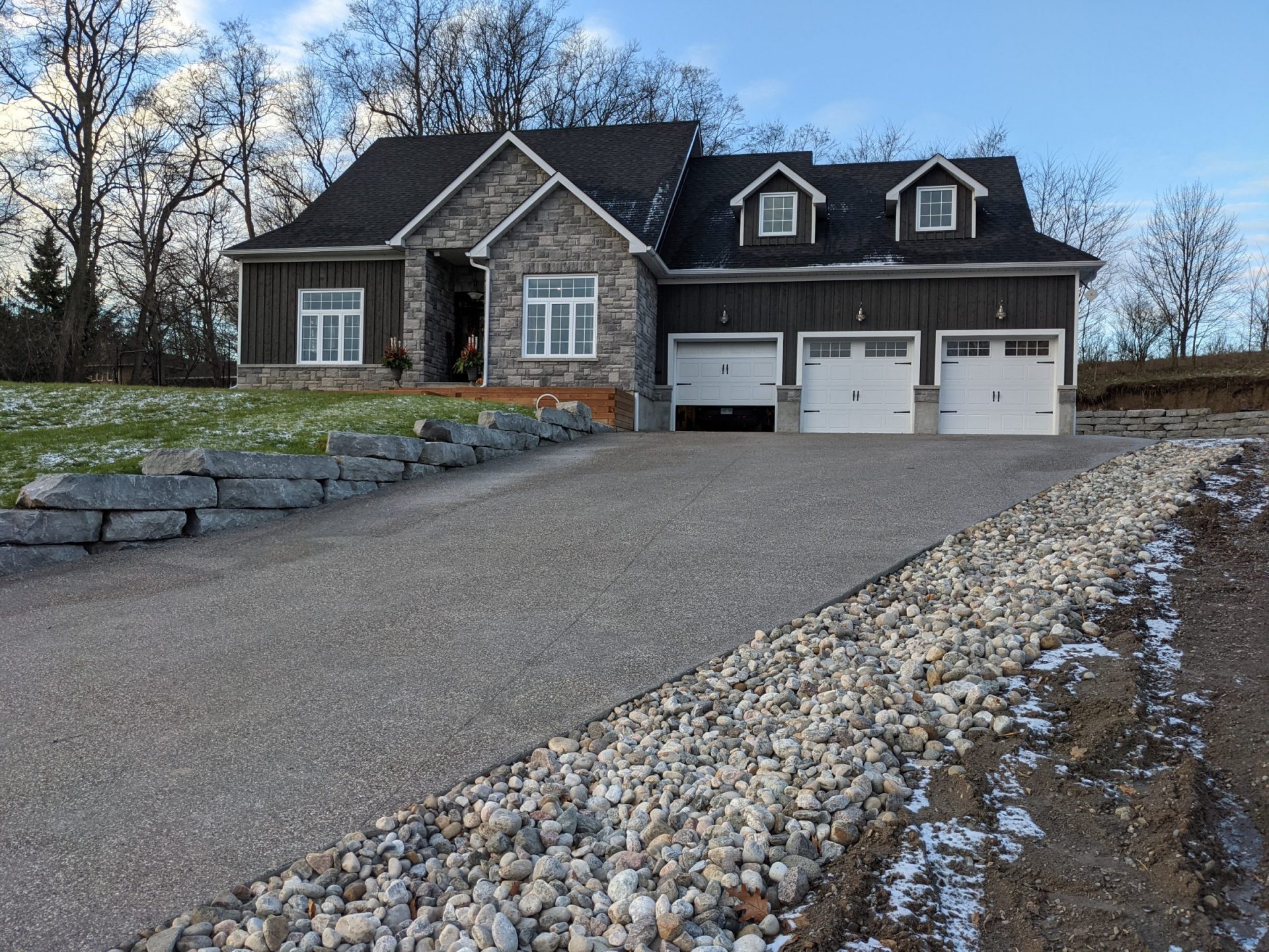 Modern stone house with three-car garage and driveway.
