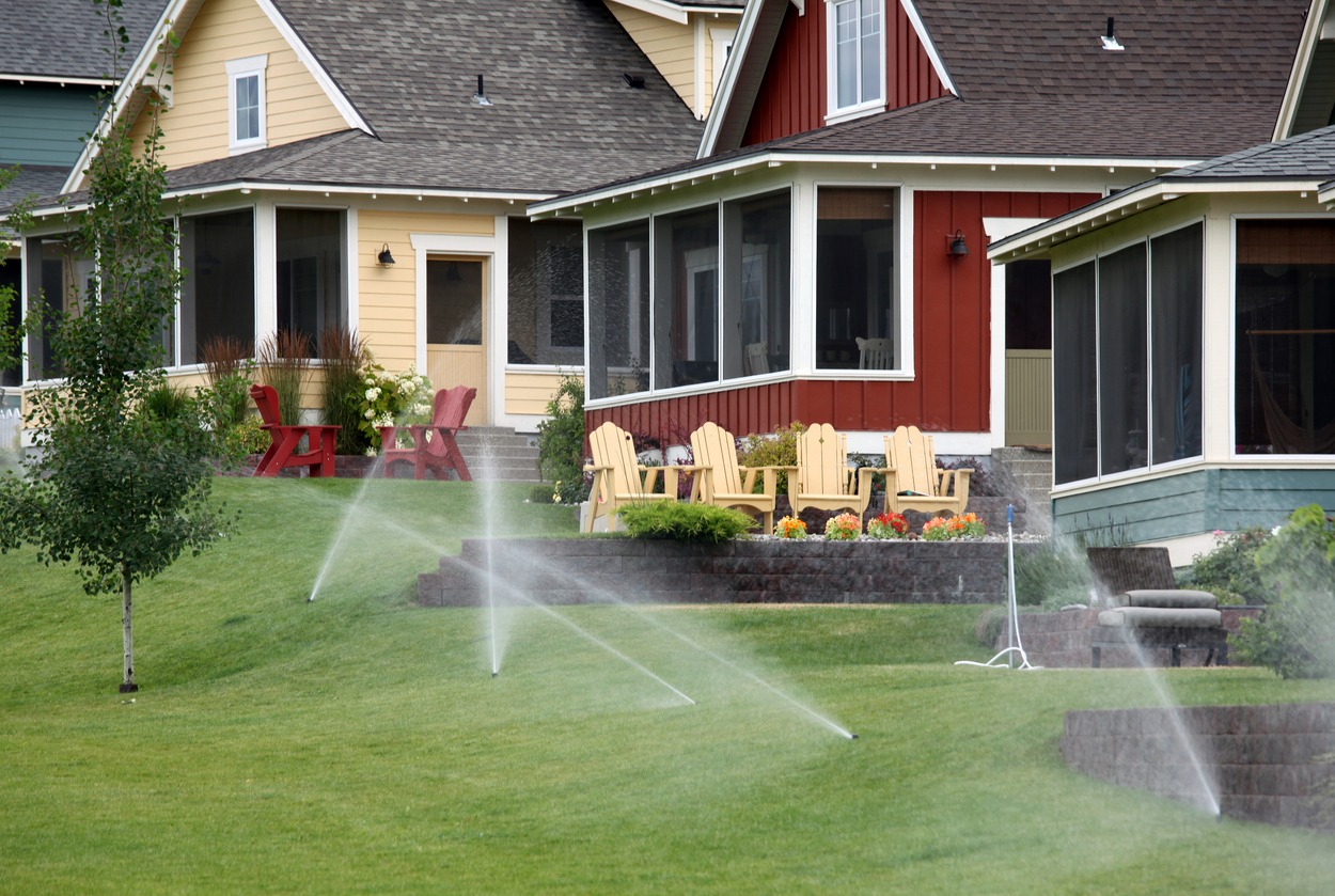 Sprinklers watering lawn in front of colorful houses.